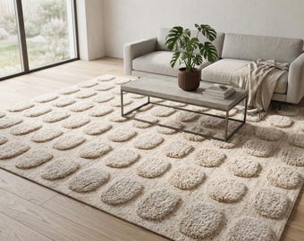 May include: A beige rectangular area rug with a repeating pattern of raised, oval-shaped tufts. The rug is placed in a living room setting, with a gray sofa, coffee table, and potted plant visible in the background.