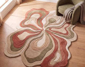 May include: An area rug with an irregular, organic shape featuring a layered, topographical pattern. The design consists of concentric, wavy bands in shades of terracotta, sage green, cream, and beige, creating a textured, multi-dimensional look.