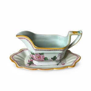 May include: A decorative gravy boat and underplate set. The pale green ceramic pieces are adorned with pink floral patterns and gold edging. The gravy boat has a handle and spout, and the underplate has a scalloped edge.
