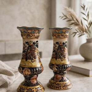 May include: A pair of matching ceramic vases featuring a flared, scalloped rim and a slender neck. The surface is decorated with intricate, multi-coloured patterns, including gold accents, floral motifs, and a central figure on horseback.