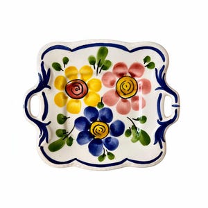 May include: A rectangular ceramic serving tray with a white base, decorated with hand-painted floral designs in yellow, pink, and blue. The tray has a scalloped edge with a blue border and handles. The flowers have red and yellow centres.