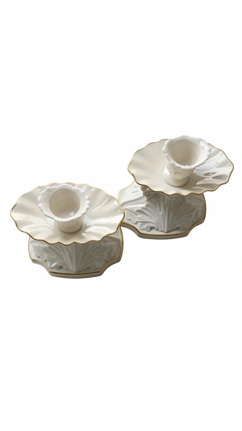 May include: Two white ceramic candle holders featuring a scalloped, flower-like top edge and a base with embossed leaf-like patterns. Each holder is finished with a thin gold trim along the edges of the top plate and the base perimeter.