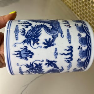 May include: White ceramic cylinder with blue dragon and cloud designs. The detailed artwork features a traditional Asian aesthetic. The cylindrical shape is accented with a blue border at the top and bottom. The design is repeated around the entire cylinder.