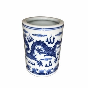 May include: A cylindrical ceramic container with a blue and white dragon design. The container features a detailed illustration of a dragon amidst clouds and flames. The top and bottom edges are accented with blue bands, creating a classic aesthetic.