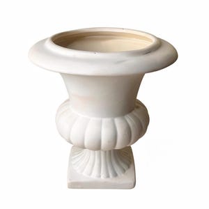 May include: A white, classical urn with a wide, flat rim and a bulbous midsection. The urn sits on a square base with a fluted design. The interior of the urn is a light beige colour.