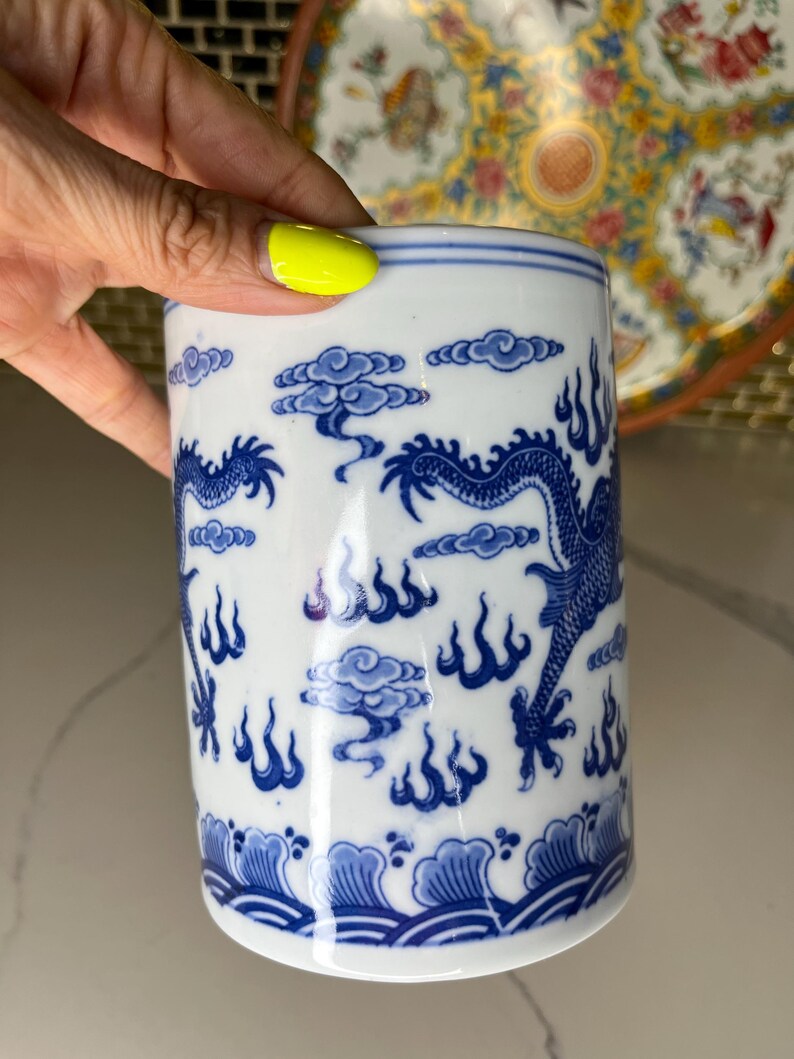 May include: White ceramic mug with a blue dragon and cloud design. The mug features a cylindrical shape and is decorated with a traditional Asian-inspired pattern. The blue and white color scheme gives it a classic and elegant look.