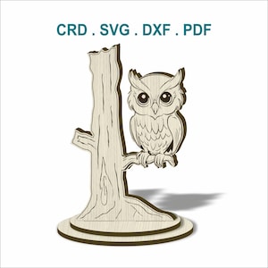 May include: A wooden owl decoration perched on a tree branch, with a tree trunk base. The owl has large eyes and detailed feathering. The text "CRD . SVG . DXF . PDF" is at the top.
