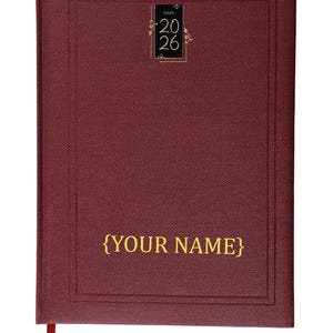 Peut inclure: Un agenda bordeaux avec des lettres dorées et un signet en ruban assorti. La couverture porte le texte "{YOUR NAME}" et un petit emblème doré avec l'année "20 26".