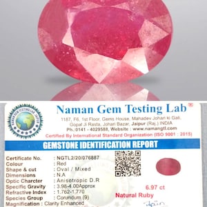 Könnte beinhalten: Ein facettierter, oval geschliffener natürlicher Rubin in leuchtendem Rot. Das Bild enthält einen Edelstein-Identifizierungsbericht vom Naman Gem Testing Lab, der die Eigenschaften des Rubins, einschließlich seines Gewichts von 6,97 Karat (ca. 1,39 Gramm), detailliert.