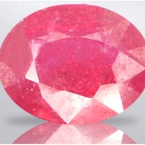 May include: A faceted, oval-cut ruby gemstone. The gem is a vibrant shade of pinkish-red, with multiple facets that reflect light. The gemstone is set against a neutral background, with a subtle reflection visible below.