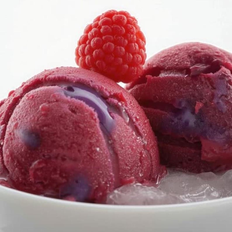 May include: Close-up of two scoops of berry-flavored ice cream in a white bowl, with a fresh raspberry on top. The ice cream is a deep red color with hints of purple. The ice cream is sitting on a bed of ice.
