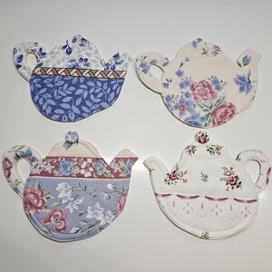 Könnte beinhalten: Vier Stoffuntersetzer in Teekannenform mit floralen Mustern. Die Untersetzer weisen verschiedene Designs auf, darunter blaue Blätter, rosa und blaue Blumen sowie ein rot-weißes Blumenmuster. Ideal für Teepartys.