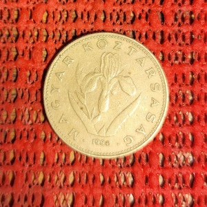 May include: A gold-colored coin with the text "MAGYAR KÖZTÁRSASÁG" around the edge and the year "1994" at the bottom. The coin features a detailed floral design in the center, set against a red background.