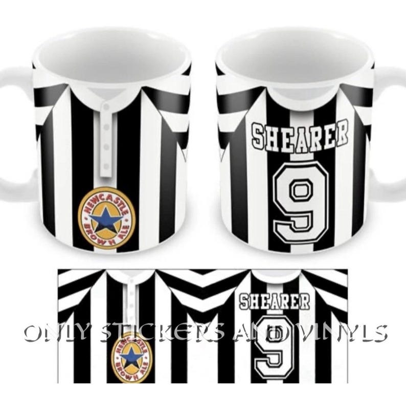 Puede incluir: Dos tazas de cer&aacute;mica blanca con un patr&oacute;n de rayas verticales negras y blancas que recuerda a una camiseta deportiva. Una taza muestra el logotipo circular de Newcastle Brown Ale con una estrella azul, la otra el nombre SHEARER y el n&uacute;mero 9.