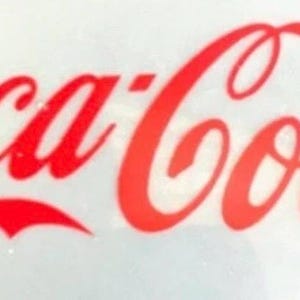Op de afbeelding: Een rechthoekig wit oppervlak met het Coca-Cola-logo gedrukt in een vet, levendig rood scriptlettertype. De iconische merknaam is horizontaal gecentreerd en toont de klassieke belettering met zijn kenmerkende vloeiende rondingen.