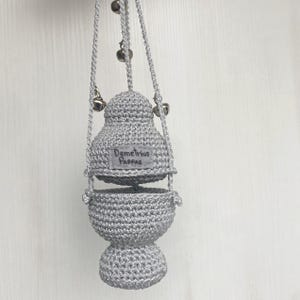 May include: A handmade, grey crocheted incense burner with the text "Demetrios Pappas" on a small label. The burner is suspended by a grey cord with small silver bells. The design features a bulbous base and a domed top.