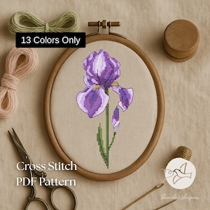 May include: A cross-stitch PDF pattern featuring a purple iris flower in a wooden embroidery hoop. The text "13 Colors Only" is displayed. Other items include scissors, thread, and a thimble.