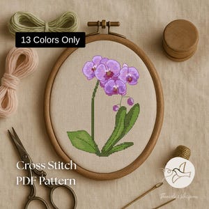 Könnte beinhalten: Ein Kreuzstich-PDF-Muster einer lila Orchidee in einem hölzernen Stickrahmen. Das Bild zeigt grüne Blätter, Stickgarn, eine Schere und den Text "13 Colors Only" und "Cross Stitch PDF Pattern".
