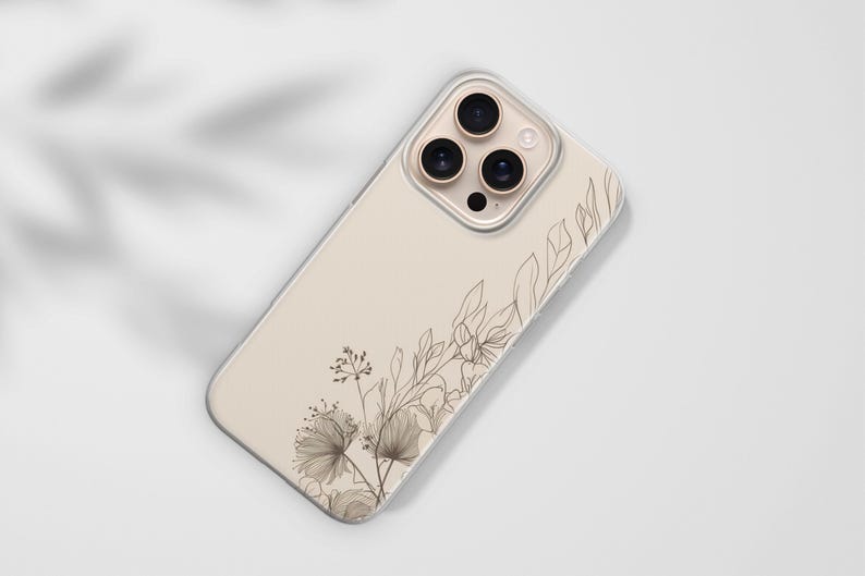 May include: A beige phone case with a floral design. The case features a clear border and a detailed illustration of delicate flowers and leaves in shades of brown. The design is on the lower left and upper right corners.