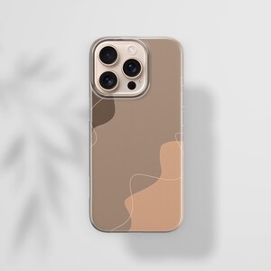 May include: A clear phone case with a brown and tan abstract design. The case has a gold camera ring and a clear border. The design features organic shapes and thin, white lines. The phone case is on a white surface.