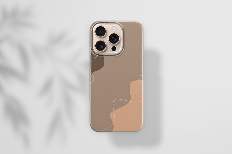 May include: A clear phone case with a brown and tan abstract design. The case has a gold camera ring and a clear border. The design features organic shapes and thin, white lines. The phone case is on a white surface.
