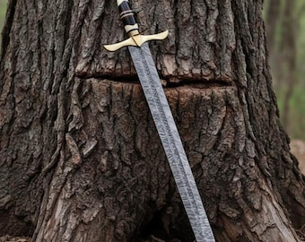 May include: A long, ornate sword with a patterned blade rests against a tree. The hilt features a gold crossguard and a handle with black, white, and gold accents. The blade has a detailed, textured design.