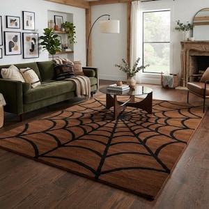May include: A rectangular area rug featuring a prominent black spider web pattern set against a solid brown background. The rug is positioned on a dark wood floor in a living room setting, covering a large portion of the floor space in front of a sofa.