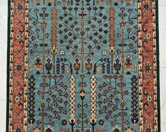 May include: Rectangular rug with a teal central field featuring a tree of life design. The border is a rust color with floral and geometric patterns, and a dark green outer edge. The rug is likely made of wool.