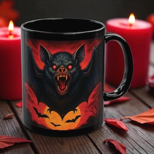 Peut inclure: Mug en céramique noire avec une illustration de chauve-souris. Le motif présente une chauve-souris menaçante aux yeux rouges, sur fond rouge et orange avec des chauves-souris et une pleine lune. Mug sur le thème d'Halloween.
