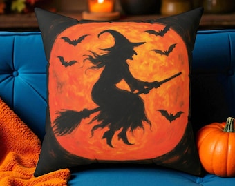 May include: Black square throw pillow featuring a silhouette of a witch on a broomstick against an orange full moon, with bats flying around. The pillow is on a blue couch with an orange blanket and a pumpkin.