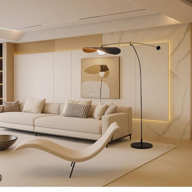 May include: Modern living room with a beige sofa, a chaise lounge, and a black floor lamp with a leaf-shaped shade. The room features a neutral color palette with a large abstract painting on the wall.
