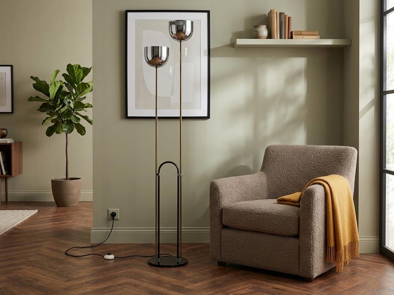 May include: A floor lamp featuring two chrome bowl-shaped shades mounted on slender vertical poles of varying heights. The lamp has a black circular base and a black arched support structure, connected to a black power cord with a floor switch.