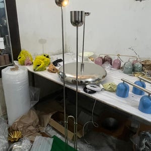 May include: A tall floor lamp featuring a polished silver metal finish with two vertical poles extending from a circular base. The lamp has two cylindrical light fixtures at different heights, each with a smooth, reflective surface and a clean design.