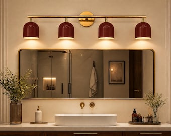 May include: A modern bathroom vanity setup featuring a rectangular mirror with a gold frame, a four-light fixture with burgundy shades, and a white oval sink. The vanity includes a wooden cabinet and decorative items.