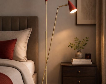 May include: A floor lamp with a gold-toned metal stand and two cone-shaped red shades. One shade points upward, while the other is adjustable and angled downward, emitting a warm light. The lamp features a circular base and a slender frame.