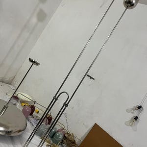 May include: A tall floor lamp featuring a polished silver-tone metal finish with two slender vertical poles connected by a U-shaped bracket. The lamp has two cylindrical light heads at the top and a circular base, providing a sleek and modern appearance.