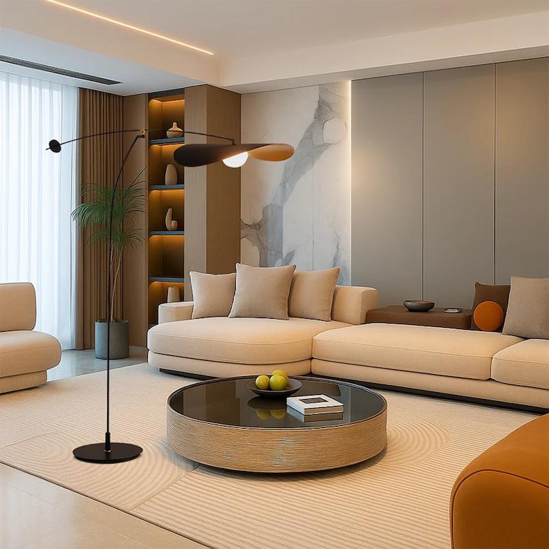 May include: A modern living room featuring a beige sectional sofa, a round wooden coffee table, and a unique floor lamp with a black and wood-toned shade. The room has a neutral color palette with a large window and a decorative wall.