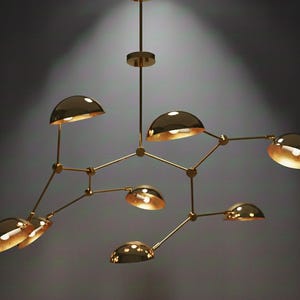 Puede incluir: Un moderno candelabro dorado con múltiples luces en forma de cúpula. La lámpara tiene una red de brazos y luces interconectados, creando un diseño de iluminación único y elegante. Las luces están posicionadas para iluminar una habitación.