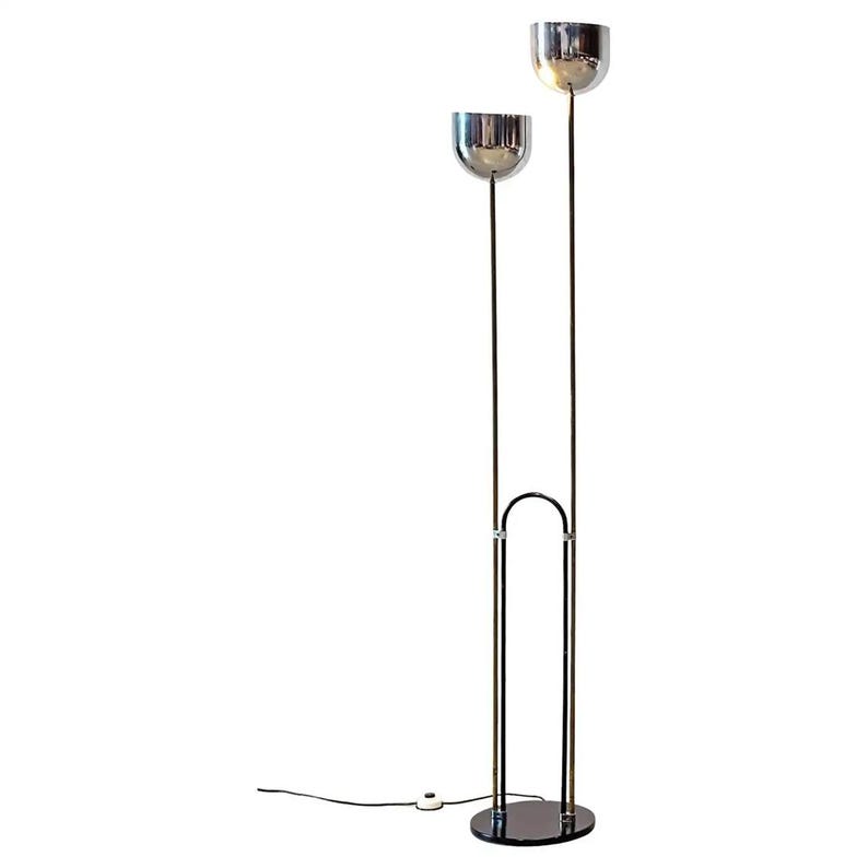 May include: A floor lamp featuring two chrome bowl-shaped shades mounted on thin vertical poles of varying heights. The structure includes a black arched support connected to a circular black base, with a black power cord and a white floor switch.