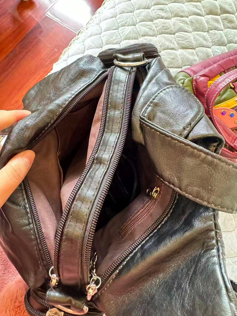 May include: A dark brown leather crossbody bag with multiple zipped compartments. The bag has a shoulder strap and silver-toned hardware. The interior lining is a lighter brown colour. The bag is open, revealing the interior.