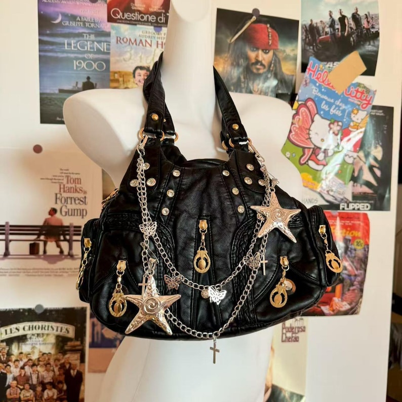 May include: Black faux leather handbag with silver-tone star and butterfly charms, studs, and zippers. The bag has a shoulder strap and multiple pockets. Movie posters are in the background.