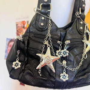 May include: Black leather handbag with silver chain and charm details. The bag has a quilted design, multiple zipped sections, and decorative charms including a starfish and flower shapes.