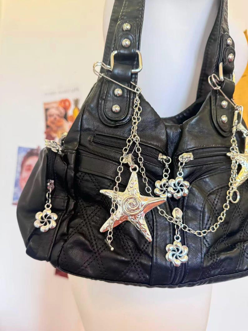 May include: Black leather handbag with silver chain and charm details. The bag has a quilted design, multiple zipped sections, and decorative charms including a starfish and flower shapes.