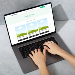 May include: A laptop displaying a website with the text "Best Digital Products." The website showcases product listings with images of landscapes. Hands are typing on the laptop keyboard.