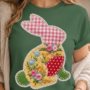 May include: Green t-shirt with a patchwork bunny design. The bunny has a pink and white gingham head, a yellow body with floral embroidery, and a red heart with white stars. The design is outlined with white pearls.