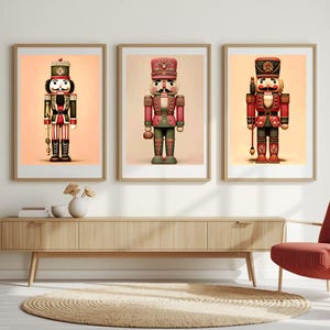 Puede incluir: Tres impresiones enmarcadas de figuras decorativas de cascanueces en rojo, verde y negro. Los cascanueces se muestran en fila, cada uno con un diseño único. Los marcos son de color marrón claro y el fondo es de color melocotón claro.