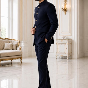 May include: A dark navy blue suit featuring a mandarin collar jacket with four gold-toned buttons down the front and matching trousers. The jacket includes long sleeves with gold-toned buttons at the cuffs and two side pockets, paired with black shoes.