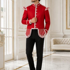 Pode incluir: Um casaco de estilo militar em vermelho vivo com gola alta, botões prateados e detalhes em branco nos ombros e na bainha, combinado com calças pretas lisas e sapatos sociais pretos. O casaco apresenta detalhes estruturados nos ombros.