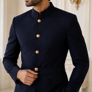 May include: A dark navy blue blazer featuring a high mandarin collar, long sleeves, and a front button closure with four polished gold-tone buttons. The jacket includes a matching integrated waist belt and two flap pockets on the lower front.