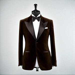 May include: A brown velvet tuxedo jacket with black satin lapels, a white dress shirt, and a black bow tie. A white pocket square is visible in the chest pocket. The jacket is displayed on a black mannequin.